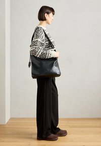 Black woven leather handbag with a smooth texture, featuring a shoulder strap, displayed alongside a patterned sweater and wide-leg pants.