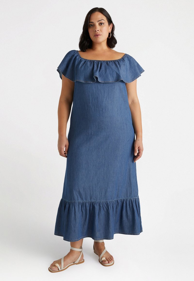 Jeans-Maxi-Kleid mit einem Rüschenausschnitt, der schulterfrei ist, einem taillierten Oberteil und einem ausgestellten Saum. Es hat eine glatte Textur in einem dunklen Blauton.