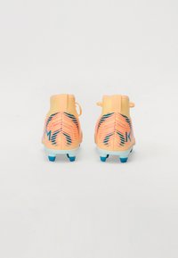 Ghete de fotbal în nuanțe de piersică, cu un upper din plasă texturată, accente întunecate contrastante și năsturei albaștri. Au un design cu gleznă înaltă și tab de călcâi.