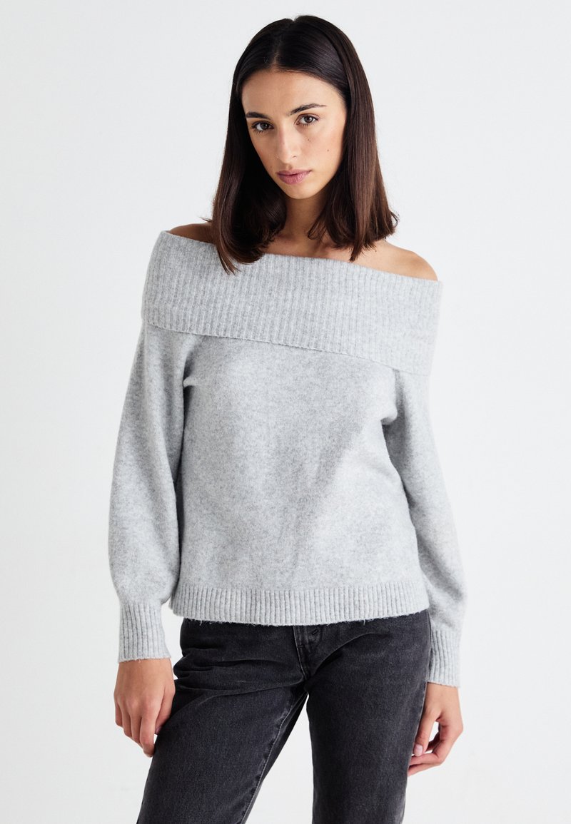 Light gray off-the-shoulder sweater with ribbed neckline, long sleeves, and soft texture, paired with dark jeans.