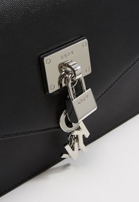 Borsa a tracolla in pelle nera texture con hardware in argento, dotata di un ciondolo a forma di lucchetto e chiave. Presenta un design angolare e una finitura elegante.