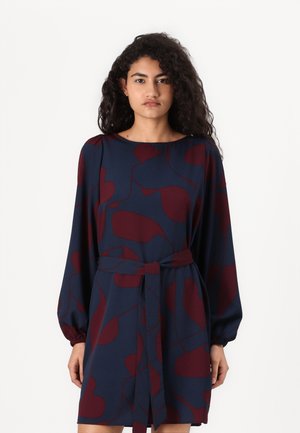 Laivansininen mekko, jossa on viininpunaisia abstrakteja kuvioita, pitkät puffihihat ja sidottava vyö. Pehmeää kangasta ja pyöreä pääntie.