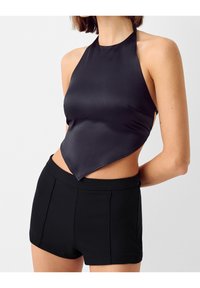 Svart satin halterneck-topp med spetstulip, kombinerad med skräddarsydda svarta shorts med platt midja och två framstående veck.