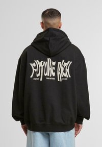Sudadera negra con un corte holgado, que presenta un gran texto blanco en la parte posterior que dice "FUTURE RICH" y detalles adicionales abajo.