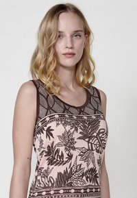 Débardeur sans manches de couleur rose pâle avec des motifs et accents de feuilles marron foncé. Possède un col rond et un design imprimé sur le tissu.