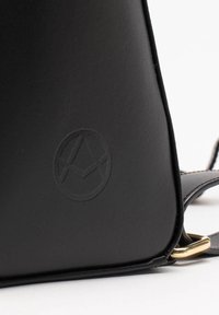 Borsa nera in pelle con una texture liscia, caratterizzata da un logo geometrico in rilievo, dettagli in acciaio dorato e un design minimalista.