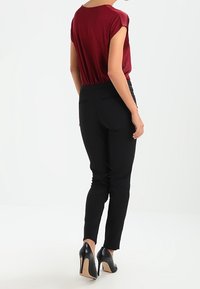 Maglietta rossa a maniche corte con vestibilità rilassata abbinata a pantaloni neri slim-fit e scarpe con tacco alte nere. Texture morbide e dettagli minimi.