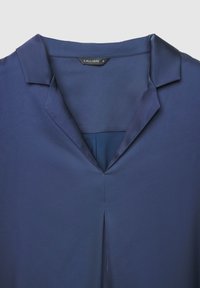 Blouse en soie bleu marine avec col pointu, encolure en V et détail d'un pli central. L'étiquette indique "CALLIOPE."
