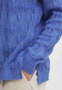 Maglione blu lavorato a maglia con motivo geometrico, polsini a coste e finitura testurizzata, realizzato in un filato morbido.