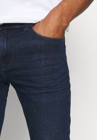 Mörkblå denimjeans med slim fit, som har subtil tonal sömnad och en framficka, och visar ett mjukt, texturerat tyg.