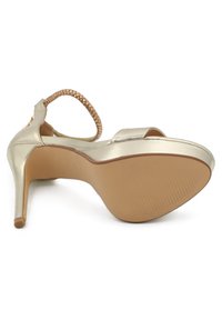 Scarpa con tacco alto in metallo dorato, con cinturino intrecciato alla caviglia e punta aperta. Texture liscia, tacco sottile e suola con motivo per una migliore aderenza.