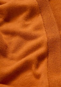 Orange knitted fabric featuring a smooth texture with ribbed detailing along one edge. The material appears soft and flexible.