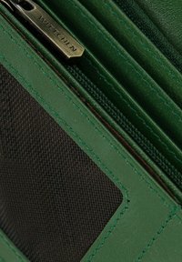 Portafoglio in pelle verde con chiusura a zip, caratterizzato da un pannello in rete nera e dettagli di cucitura orizzontale. Hardware della cerniera in tonalità oro visibile.