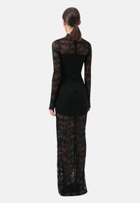 Zwarte kanten jurk met lange mouwen, nauwsluitend lijfje en doorschijnende lange rok met bloemmotieven. Ontwerp met open rug.