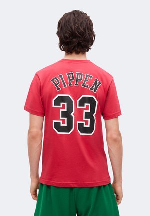 Persona che indossa una maglietta rossa con "PIPPEN" e il numero 33 in grandi lettere nere e bianche sulla schiena, abbinata a pantaloncini verdi.