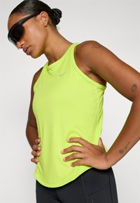 Neon grøn atletisk tanktop med rund hals og flade sømme. Har et lille gråt logo og et glat, svedtransporterende stof.