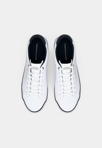 White lace-up sneakers with a smooth leather upper, contrast black sole, and "TOMMY HILFIGER" branding on the tongue.