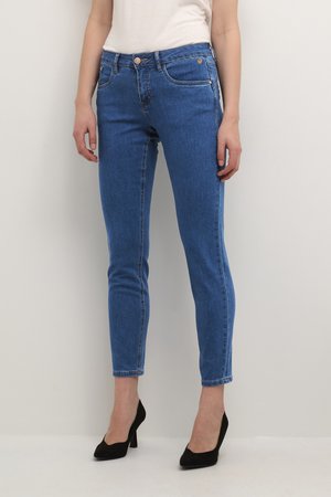 Jean skinny en denim bleu avec cinq poches, design ajusté, coutures contrastantes et fermeture éclair avec bouton. Associé à des talons noirs.