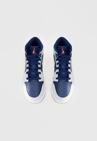 Ψηλές αθλητικές μπότες από ναυτικό μπλε και ανοιχτό γκρι δέρμα. Τεχνικό υφασμάτινο τζακέτο, πορτοκαλί λογότυπο, τρυπητό μπροστινό μέρος και αντιθετικά κορδόνια.