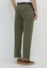 Olivgrüne Cargo-Hosen mit geradem Schnitt, zwei Gesäßtaschen und Knopfverschluss. Getragen mit braunen Wildlederschuhen und einem schwarzen Gürtel.