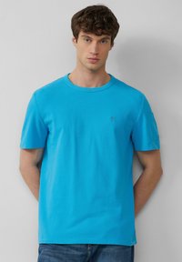 Felle blauwe katoenen T-shirt met ronde hals en korte mouwen. Bevat een klein logo op de borst en een textuurdetail op de schouders.