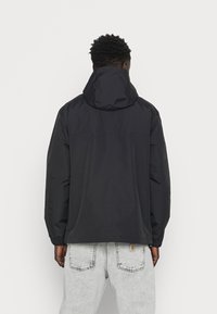 Black waterproof jacket with a hood, featuring elastic cuffs and a relaxed fit. Smooth texture with a simple, minimalistic design.