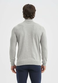 Pull en maille grise à col roulé avec des manches longues, silhouette ajustée et poignets côtelés. Texture lisse et design minimaliste.