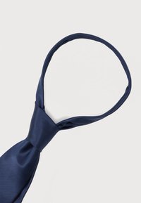 Cravate en soie bleu marine nouée en nœud Windsor sur fond blanc uni.