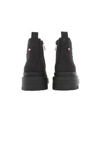 Black suede ankle boots with a chunky rubber sole, featuring a side zipper and a small French flag emblem on the heel.