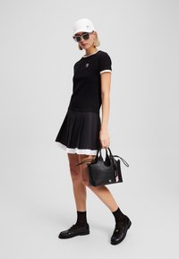Black t-shirt with white trim, pleated black skirt with white underlayer, black bag with handle, and black shoes, paired with a white cap and sunglasses.