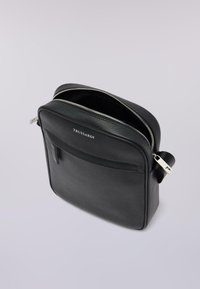 Borsa a tracolla in pelle nera con superficie strutturata, chiusura con zip, tasca frontale e dettagli in metallo argentato. Nome del marchio "Trussardi" visibile sul davanti.