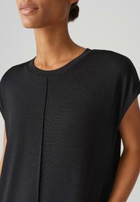 Zwarte top met korte mouwen van een zachte, gemêleerde stof, met een ronde halslijn en een subtiele plooidetail aan de voorkant. Getailleerde pasvorm die aan de zijkanten verstelbaar is.