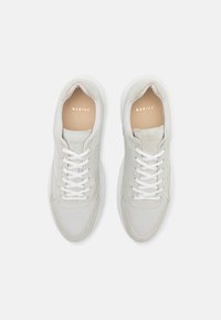 Zapatillas blancas de nubuck con acentos de ante, que presentan cordones blancos, una suela acolchada y un logo dorado "NUBIKK" en la plantilla.