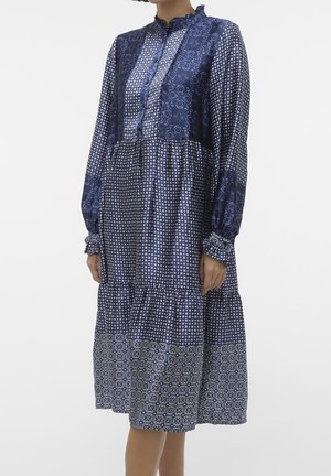 Robe à manches longues bleu marine avec un mélange de motifs géométriques, patte de boutonnage, col volanté et jupe à volants. Texture semblable à la soie.
