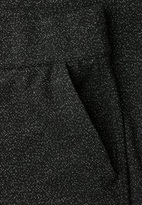 Tissu noir avec une surface texturée comportant de petites taches blanches. Le design comprend un ourlet plié et un détail de poche discret.