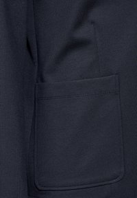 Mörk marinblått tyg med en slät yta. Har en ficka med raka kanter och precisa sömmar, mot en enhetlig bakgrund.