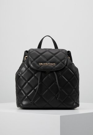 Černý prošívaný kožený batoh Valentino s uzavíráním na stahovací šňůrku a horní klopou, vystavený na bílém podstavci na jednoduchém pozadí.