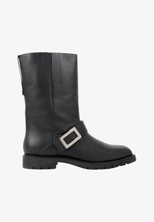 Botte en cuir noir mi-mollet avec un talon bas et une large bride avec une boucle carrée argentée autour de la cheville.