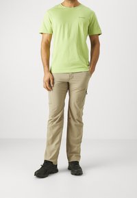 Pánské světle zelené bavlněné tričko s krátkým rukávem, kombinované s béžovými cargo kalhotami se zipovými kapsami a černými outdoorovými botami.