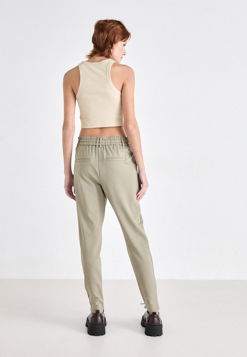 Beige, kurz geschnittenes Tanktop, kombiniert mit hellgrünen, elastischen Hosen mit einer taillierten Beinform. Die Hosen verfügen über zwei Gesäßtaschen.