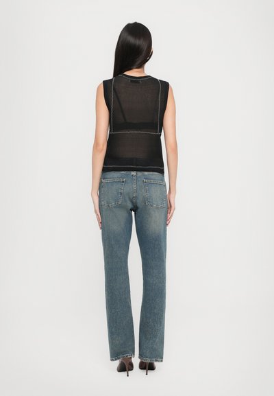 Débardeur noir sans manches avec une texture transparente et des détails de couture blancs, assorti à un jean droit bleu clair avec des poches arrière.