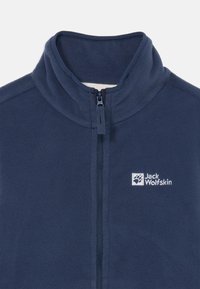 Tumesinine fliisjakki, millel on kõrge krae, lukuga esikülg ja vasakul küljel närvitud "Jack Wolfskin" logo. Pehme tekstuur.