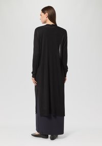 Długi czarny kardigan wykonany z lekkiego materiału dzianinowego, o luźnym kroju, z bocznymi rozcięciami i długimi rękawami. Prosty design, bez wzorów.
