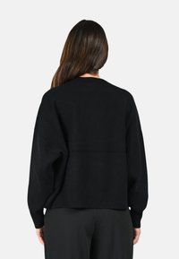 Pull noir à la coupe décontractée, avec des manches longues et un ourlet côtelé. Texture douce, design simple, sans motifs ni éléments métalliques visibles.
