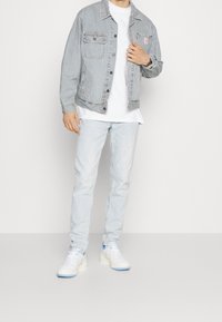 Randig denimjacka med två bröstfickor, paired med en vit t-shirt och ljusblå jeans. Vita sneakers med blå detaljer fulländar outfiten.