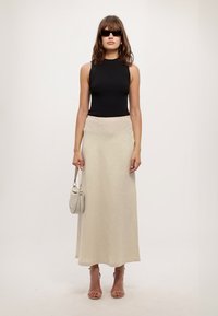 Top in morbido cotone nero a coste, lunga gonna beige, sandali con tacco trasparente, piccola borsa grigia e occhiali da sole scuri. Design semplice e aderente con texture morbide.