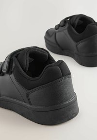 Schwarze Sportschuhe mit einem glatten, synthetischen Obermaterial, Stofffutter, gepolstertem Schaft und verstellbarem Riemen; ausgestattet mit einer strukturierten Gummisohle.