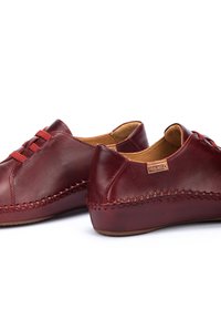 Zapatos de cuero rojo con forma redondeada, costuras decorativas a lo largo de la suela y un diseño de cordones simple. Interior forrado con material color tostado.