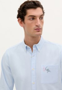 Lichtblauwe button-up shirt van katoen, met een borstzak met geborduurde details, waaronder een doodskop en de letters "SC."
