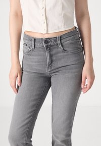 Jeans de mezclilla gris con un diseño ajustado, estilo de cinco bolsillos y cierre de botón. Tejido ligeramente texturizado con un ligero estiramiento para mayor comodidad.